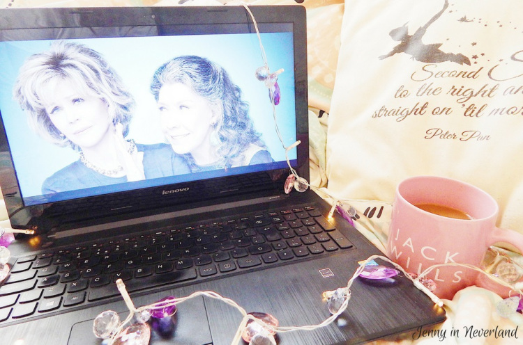 Laptop showing Grace and Frankie, resting on a bed with fairy lights and a cup of tea in a Jack Wills mug