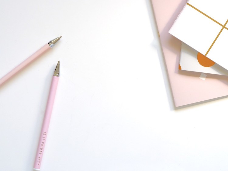A white desk, with pink pens and pink and white notebooks