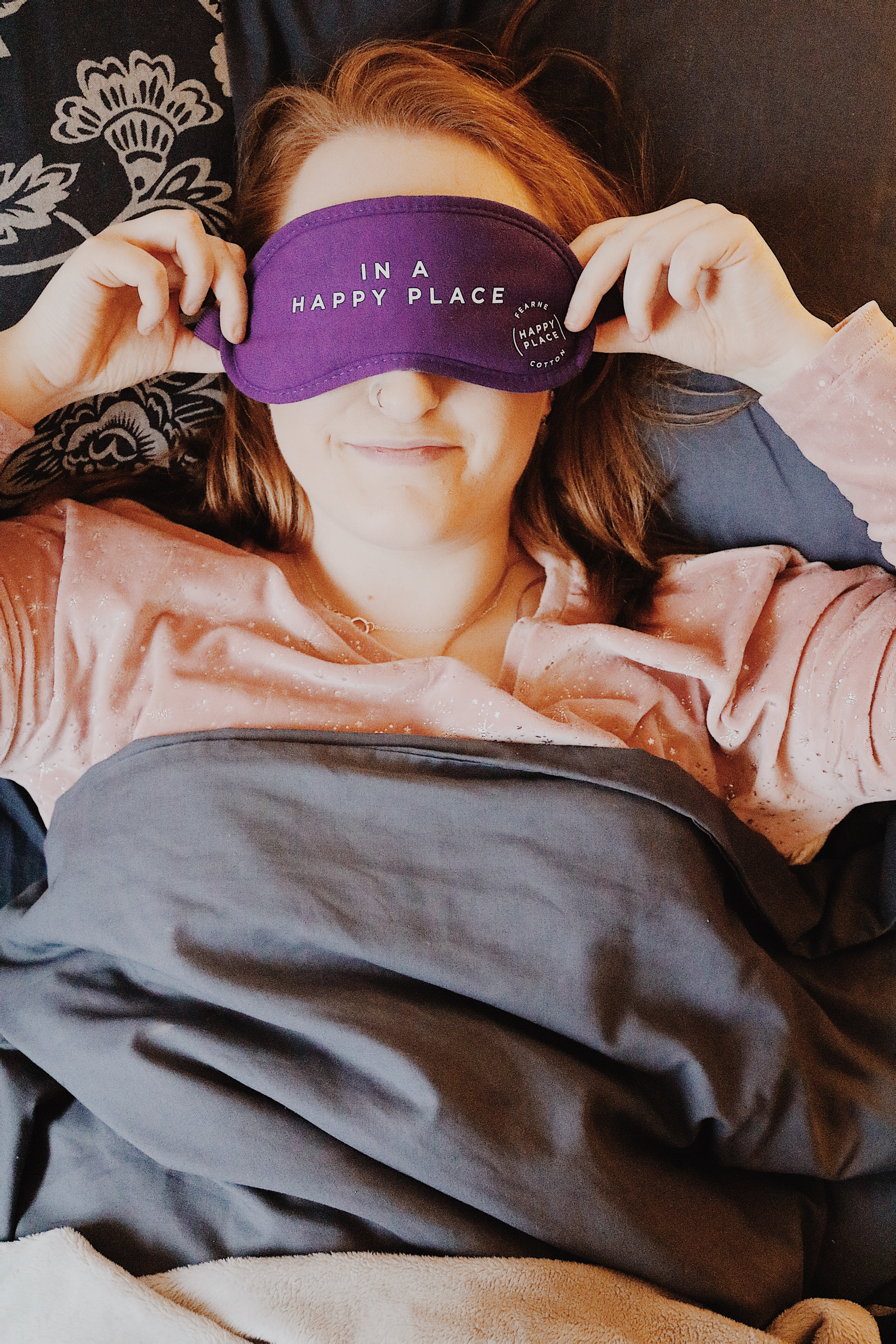 How To Switch Off and Relax: A girl laying in bed under the covers wearing a sleeping mask saying "In my happy place"